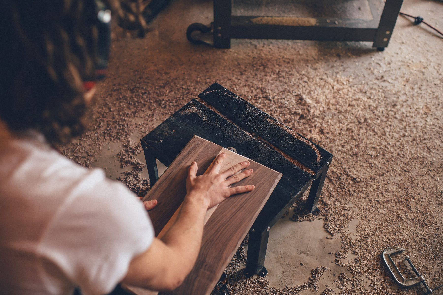 Mani che levigano una tavola di legno scuro sul banco, tra la segatura
